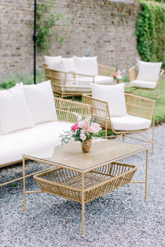 rattan couch and chairs with white cushions and a rattan table with a small pink floral arrangement