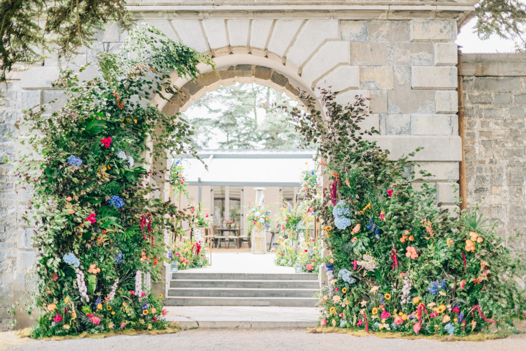 stone archway decorated with floral arch and greenery in bright colors