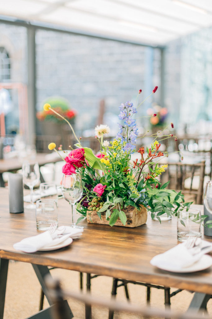 small floral arrangement with bright pink yellow and blue flowers and greenery in a wooden pot